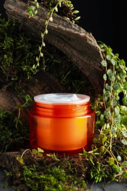 Kavanoz dolusu nemlendirici vücut kremi, ağaç kabuğu ve bitkiler gri masada, yakın plan.