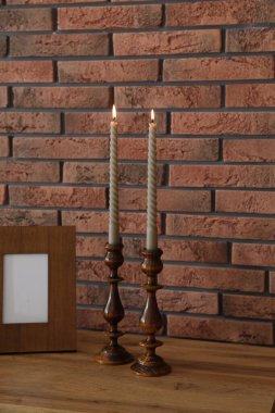 Mum ve tuğla duvarın yanındaki masada yanan mumlar.