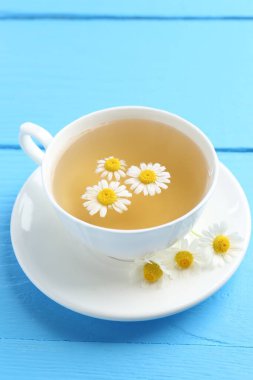 Fincanda nefis papatya çayı ve açık mavi ahşap masada taze çiçekler, yakın plan.