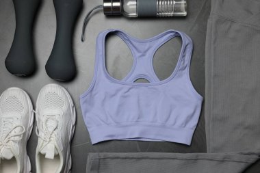 Spor kıyafetleri, spor ayakkabıları, dambıllar ve su şişesi gri arka planda, düz yatıyordu.