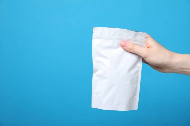 Açık mavi arka planda fermuarlı stand-up kesesi olan kadın, yakın plan. Tasarım için model