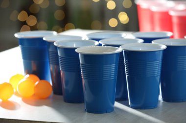 Plastik bardaklar ve toplar açık ahşap masada bulanık ışıklara karşı, yakın plan. Bira pong oyunu
