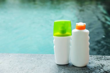 Dışarıdaki yüzme havuzunun yakınındaki taş yüzeyde güneş koruma ürünleri şişeleri, metin için yer.