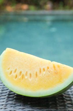 Açık havuz kenarında hasır masada lezzetli bir karpuz dilimi, yakın plan.