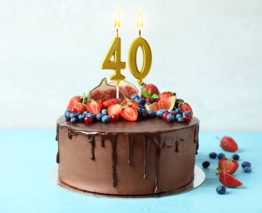 Meyveli çikolatalı kek ve açık mavi masada yanan mumlar. 40. yaş günü veya başka özel bir gün.