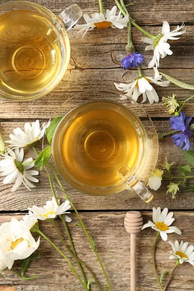 Cam fincanlarda aromatik bitki çayı ve tahta masada çiçekler.