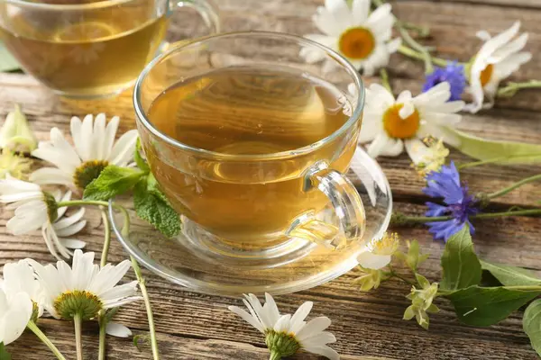 Cam bardaklarda aromatik bitki çayı, ahşap masada nane ve çiçekler, yakın plan.