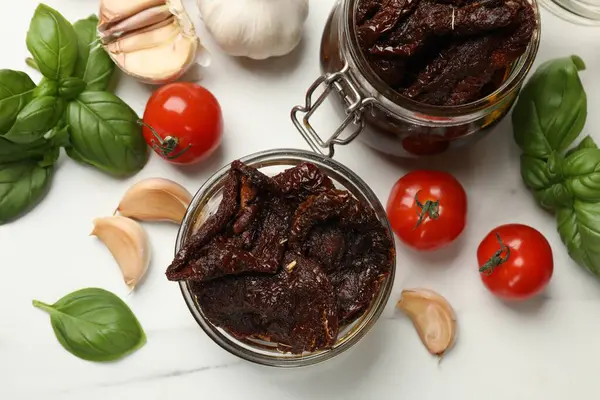 Lezzetli güneşte kurutulmuş domatesler, taze sebzeler, fesleğen ve sarımsak beyaz masada, düz yatıyordu.