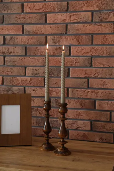 Mum ve tuğla duvarın yanındaki masada yanan mumlar.