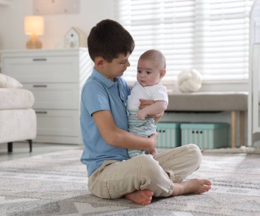 Evde yerde kucaklaşan sevimli küçük kardeşler.