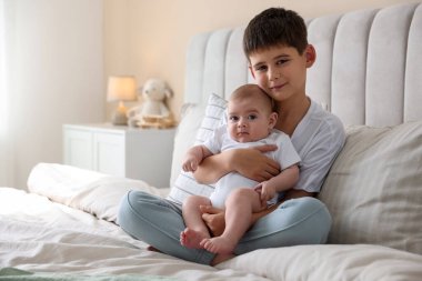 Evdeki yatakta oturan sevimli küçük kardeşler.