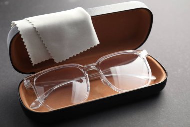 Gri arka planda şık gözlüklü ve temizlik bezli çanta, yakın plan.