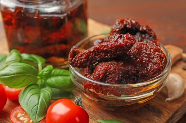 Lezzetli güneşte kurutulmuş domatesler, taze sebzeler, fesleğen ve sarımsak ahşap masada, yakın plan.