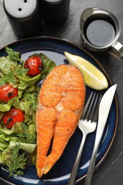 Deniz ürünleri. Siyah masada salata ve limonla servis edilen lezzetli somon bifteği.