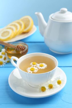 Lezzetli papatya çayı, taze çiçekler, limon ve bal açık mavi ahşap masada, yakın plan.