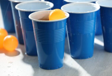 Plastik bardaklar, alkollü içecekler ve açık ahşap masada toplar, yakın plan. Bira pong oyunu