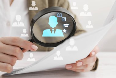 Çalışan araması. Kadın masadaki büyüteçle belgeye bakıyor, yakın plan. Aday olarak insan simgeleri