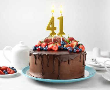 Meyveli çikolatalı kek ve beyaz masada yanan mumlar. 41. yaş günü veya başka özel bir gün.