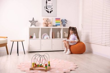 Küçük kız oyun odasında pouf hakkında kitap okuyor.