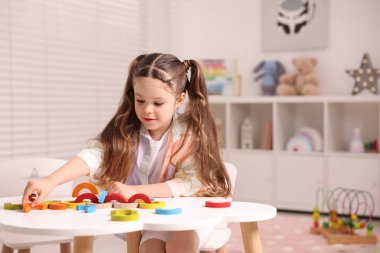 Motor beceri geliştirme. Beyaz masada renkli ahşap parçalarla oynayan küçük bir kız.