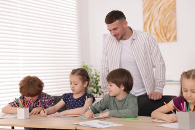 Çocuklara resim dersinde resim yapmayı öğreten bir adam.