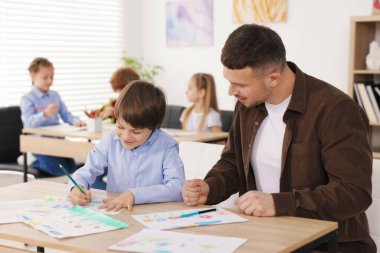 Çocuğa resim çizmeyi öğreten adam kapalı alanda resim dersi veriyor, seçici odaklanıyor.