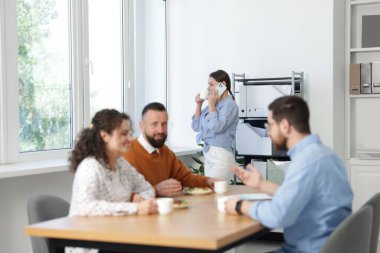 İş arkadaşları ofiste yemek yiyor ve sohbet ediyorlar.