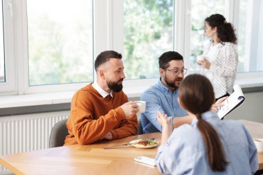 İş arkadaşları yemek yiyor ve ofiste öğle arasında iş tartışıyorlar.