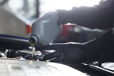 İşçi motor yağını teneke kutudan araba motoruna boşaltıyor.