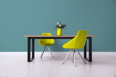 Yemek masası ve sarı sandalyeler odadaki yeşil duvarın yanında. İç tasarım