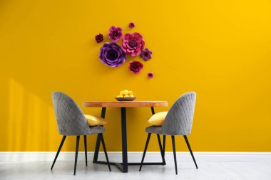 Yemek masası ve turuncu duvarın yanında gri sandalyeler. Odada çiçek dekoru var. İç tasarım