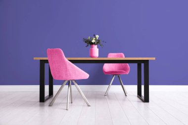 Yemek masası ve çivit renkli duvarın yanındaki pembe sandalyeler. İç tasarım