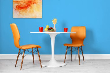 Yemek masası ve turuncu sandalyeler, açık mavi duvarın yanında. İç tasarım