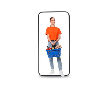 Alışveriş sepetli mutlu kadın beyaz arka planda cep telefonundan çıkıyor. Çevrimiçi sıralama