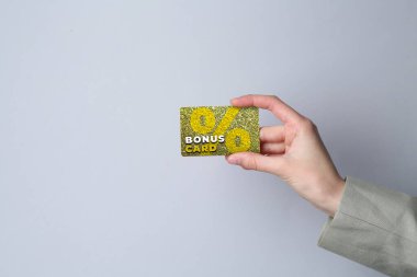 Gri arka planda şık tasarımı olan Bonus kartı tutan kadın, yakın plan.