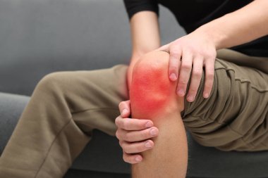 Evdeki koltukta dizinde ağrıdan muzdarip bir adam, yakın plan.