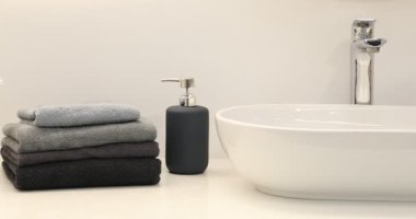 Yumuşak havlu yığını, sıvı sabun ve kasımpatı çiçekleri banyodaki beyaz tezgahın üzerinde, sola hareket eden kamera.