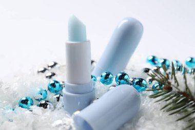 Nemlendirici dudak kremleri, Noel dekorasyonu ve yapay kar üzerindeki köknar ağacı dalları, yakın plan. Kış bakımı