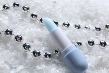 Nemlendirici dudak kremi ve yapay kar üzerine Noel süsü, yakın plan. Kış bakımı