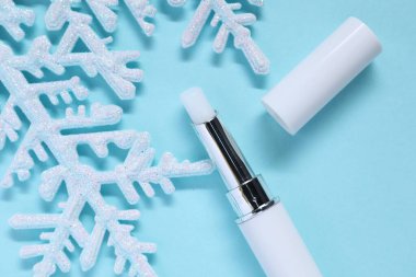 Nemlendirici dudak kremi ve açık mavi arka planda Noel dekoru, düz yatış. Kış bakımı