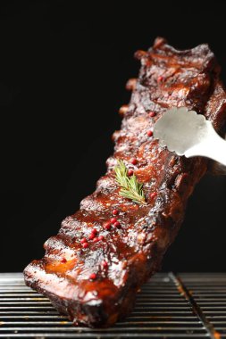 Siyah arka planda ızgaradan maşayla leziz domuz pirzolası alıp yakın plan çekiyoruz.