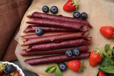 Lezzetli meyve dürümleri, çilekler, yaban mersinleri ve nane şekeri gri ahşap masada, düz uzanmış