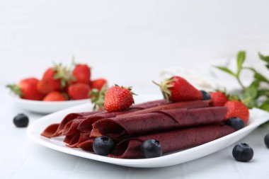 Lezzetli meyve dürümleri, çilekler ve yaban mersinleri beyaz masada, yakın plan. Metin için boşluk