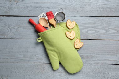 Farklı mutfak aletleri fırın eldiveni ve açık gri ahşap masa üzerinde avuç içi kurabiyeler.