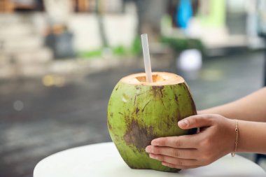 Dışarıdaki masada yeşil hindistan cevizli, ferahlatıcı içecekten içen kadın, yakın plan. Metin için boşluk