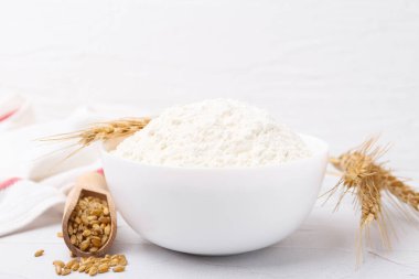 Buğday unu kasede, tahıllar ve çiviler beyaz masada, yakın plan.