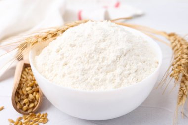 Buğday unu kasede, tahıllar ve çiviler beyaz masada, yakın plan.