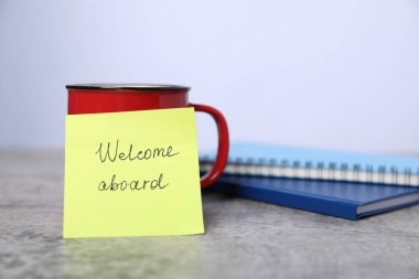 Cümle ile yapışkan not Gemiye hoş geldiniz, kahve ve defterler gri masaya, yakın plan