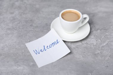 Kelimesi kelimesine yapışkan bir not Hoş geldin ve kahve gri masada, yakın plan