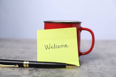 Kelimesi kelimesine yapışkan not Hoş geldin, kahve ve kalem gri masada, yakın plan